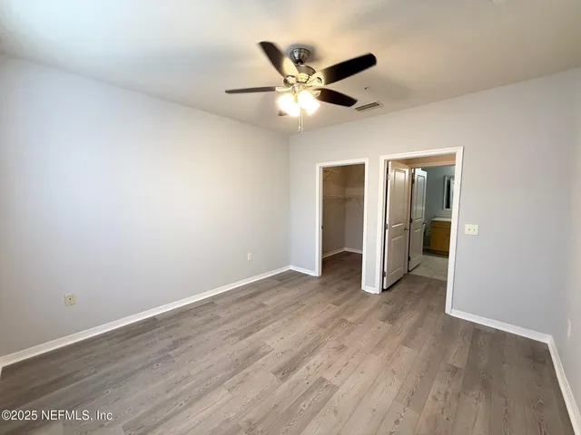 a view of an empty room with wooden floor and a ceiling fan