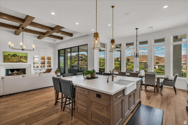 2608 Canyon Ridge Drive St. George, UT 84770 - Photo 16 of 86 Spacious open-concept living area featuring a large kitchen island with a farmhouse sink, wood-finish flooring, a fireplace, exposed ceiling beams, and expansive windows