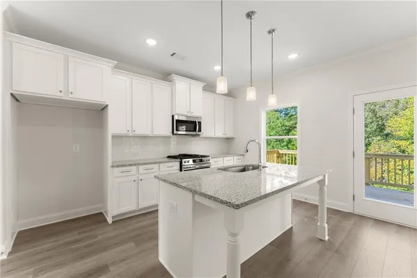 a kitchen with stainless steel appliances granite countertop a sink a stove a refrigerator and white cabinets with wooden floor