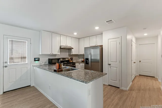 a kitchen with stainless steel appliances granite countertop a refrigerator a sink dishwasher a stove and white countertops with wooden floor