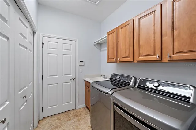 a utility room with stainless steel appliances granite countertop white cabinets and a refrigerator