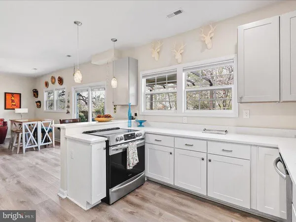 a kitchen with a stove a sink and white cabinets with wooden floor next to windows