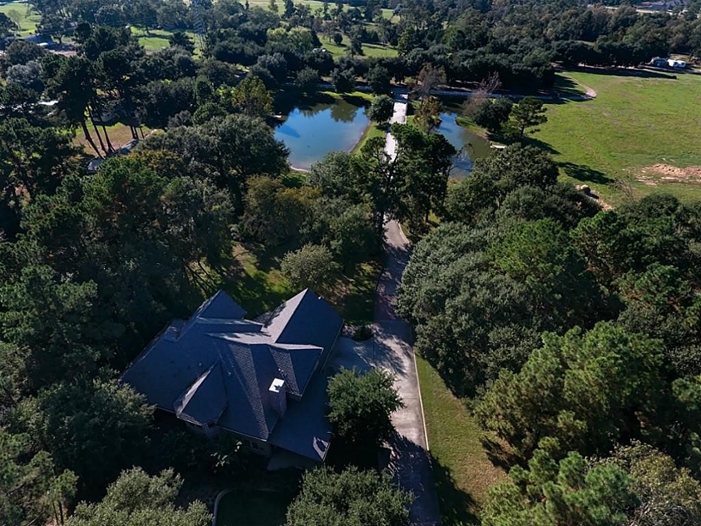 12126 Zion Road Tomball, TX 77375 - Photo 45 of 50 This breathtaking aerial view showcases an exceptional 5,080-square-foot custom estate perfectly positioned on 5.08 acres, surrounded by towering mature trees that create a private, park-like setting. A long driveway welcomes you home, leading to an impressive residence nestled among the landscape for maximum privacy & tranquility. The sparkling stocked pond serves as the centerpiece of the property, offering peaceful water views, a place to fish, or simply relax while enjoying the beauty.
