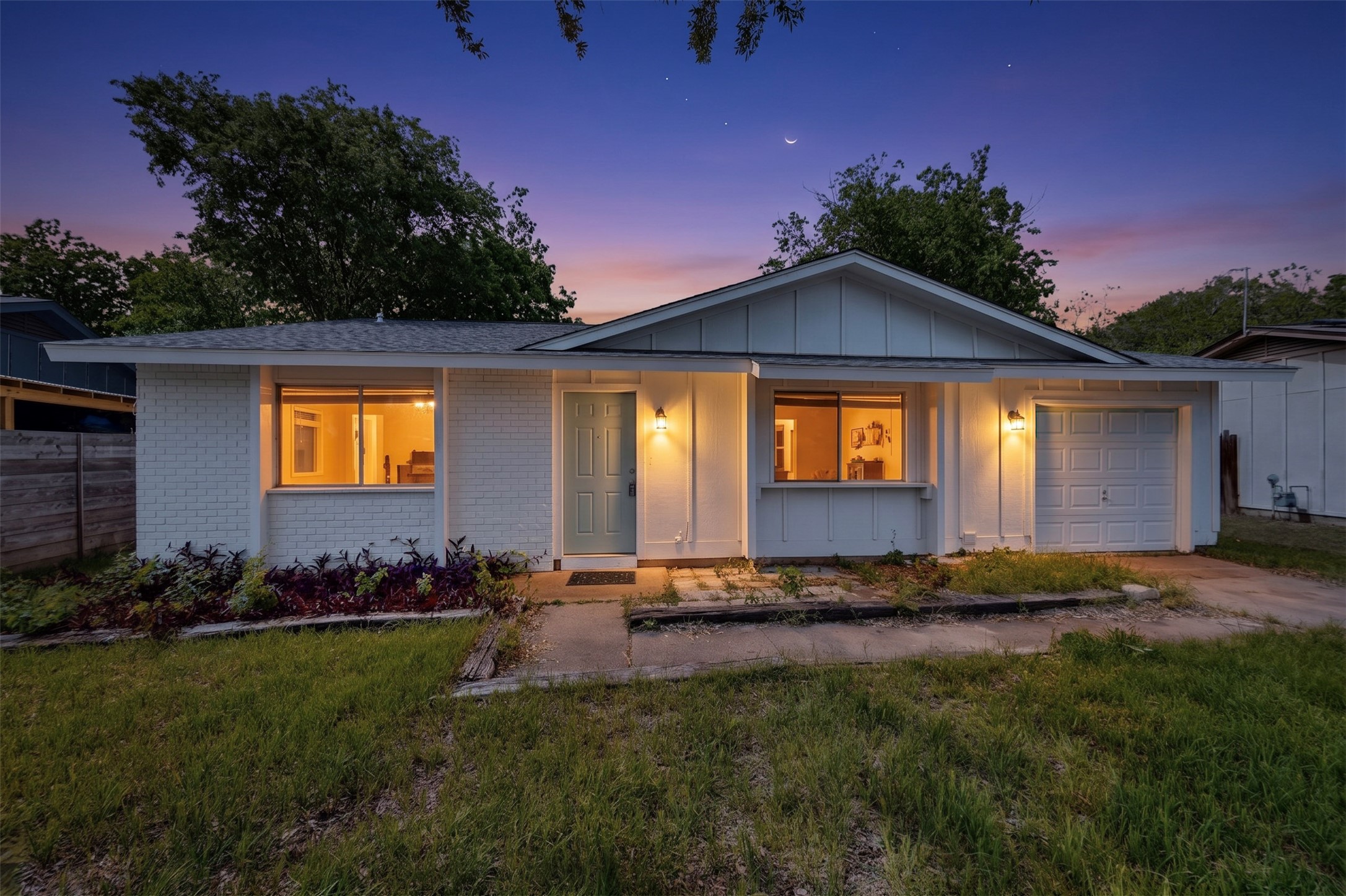 The property features a single-story design with white painted brick and vertical siding, a light blue front door, and an attached garage with a white garage door