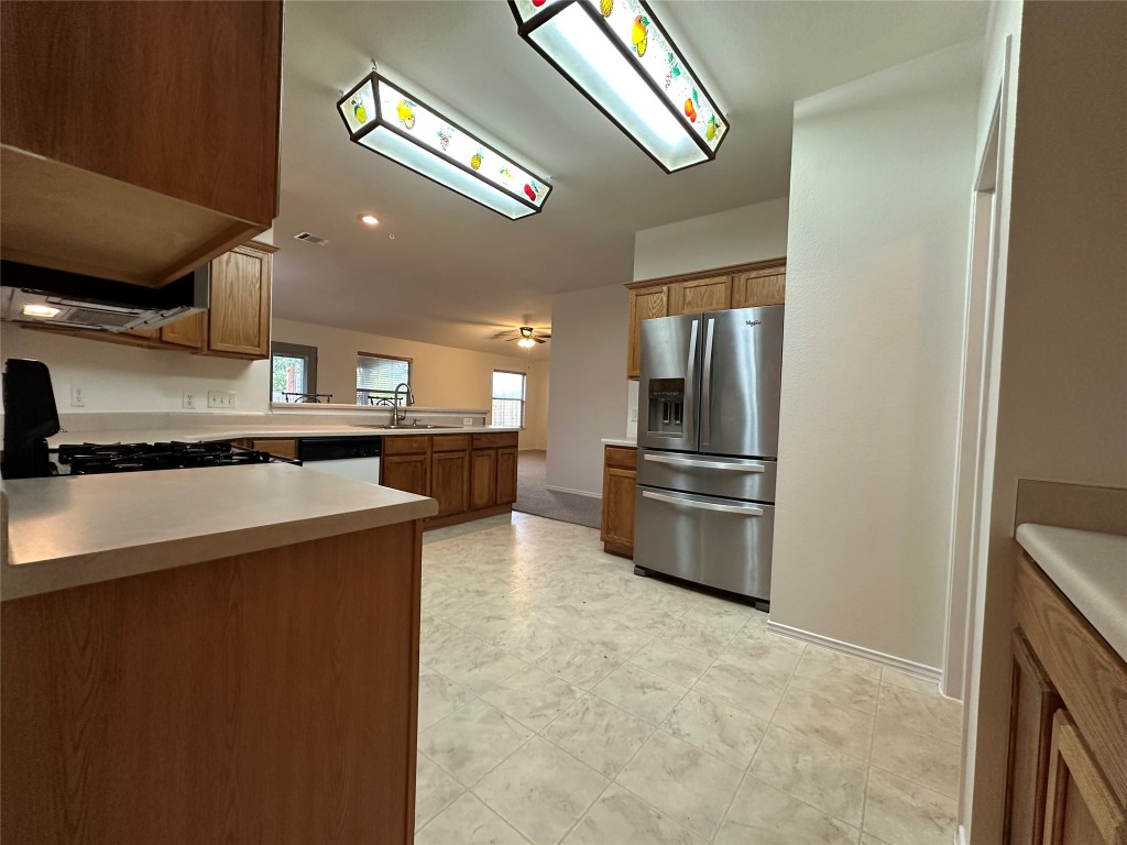 3412 Napa Valley Bend Leander, TX 78641 - Photo 17 of 27 Kitchen with stainless steel fridge, a peninsula, light countertops, brown cabinetry, and black stove