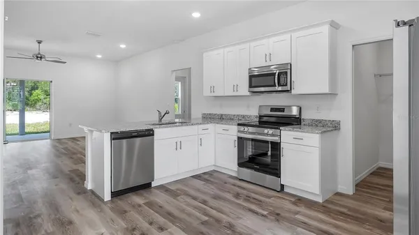 a kitchen with stainless steel appliances white cabinets a sink a stove a microwave and wooden floors