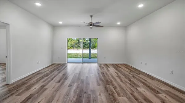 an empty room with wooden floor ceiling fan and windows