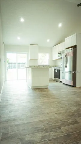 a view of kitchen and empty room with wooden floor