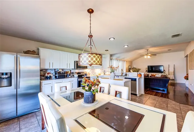 a kitchen with stainless steel appliances kitchen island granite countertop a refrigerator a stove top oven a sink dishwasher and white cabinets with wooden floor