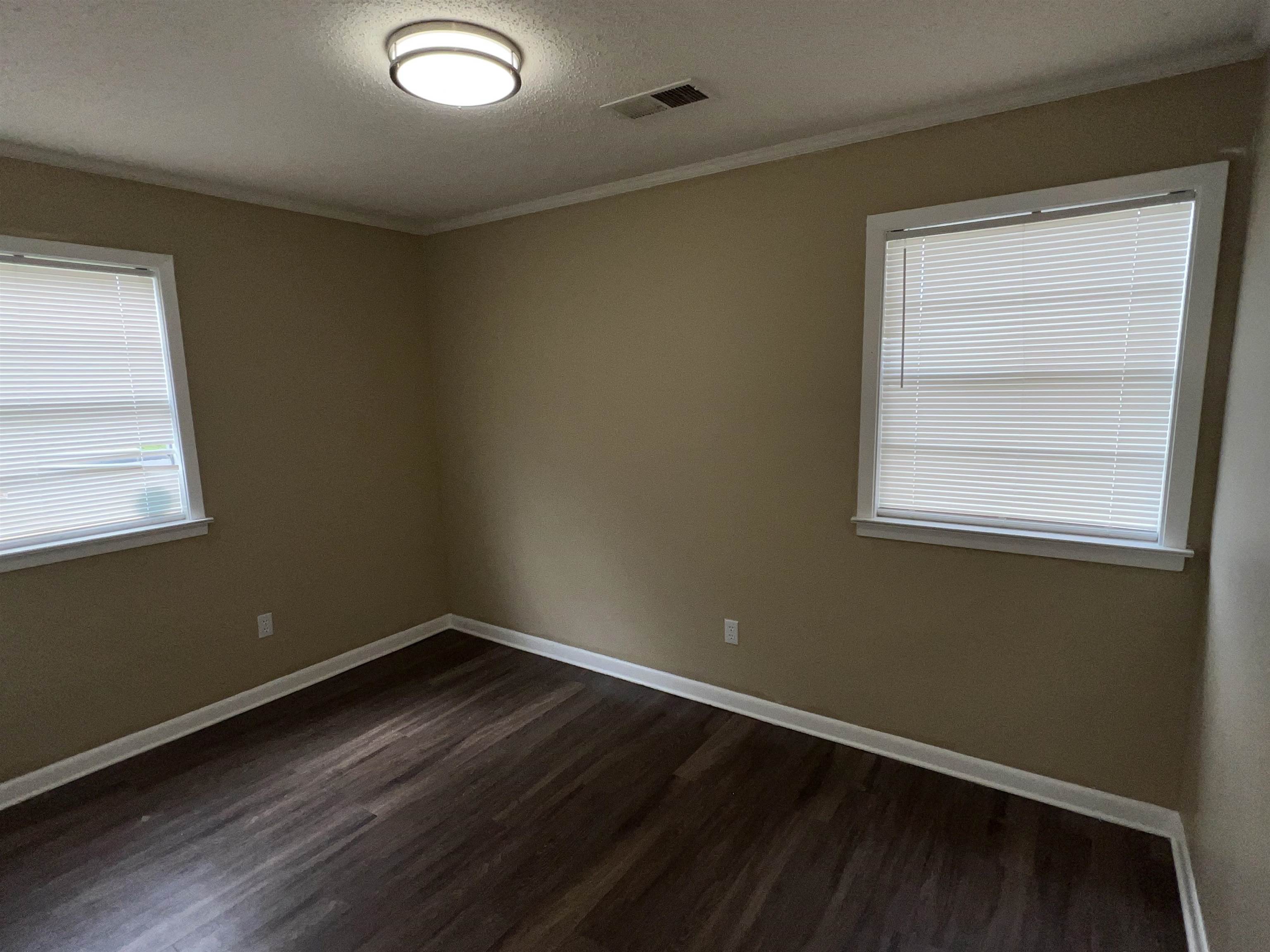 892 Restbrook Avenue Memphis, TN 38127 - Photo 5 of 11 Spare room featuring dark wood-style flooring, a textured ceiling, crown molding, and plenty of natural light