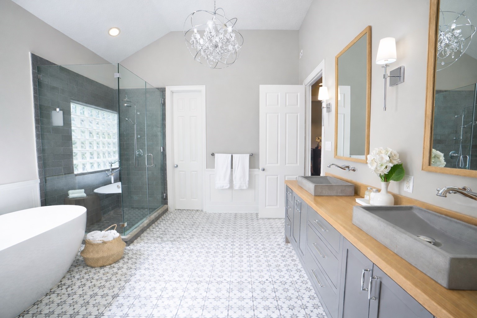 Primary bath showcases a freestanding soaking tub, oversized glass-enclosed shower, and double vanity with concrete sinks, all set atop patterned tile floors and filled with natural light.