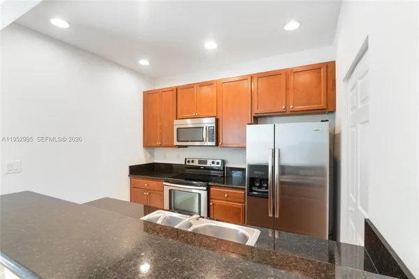 a kitchen with stainless steel appliances granite countertop a refrigerator a sink a stove and wooden cabinets