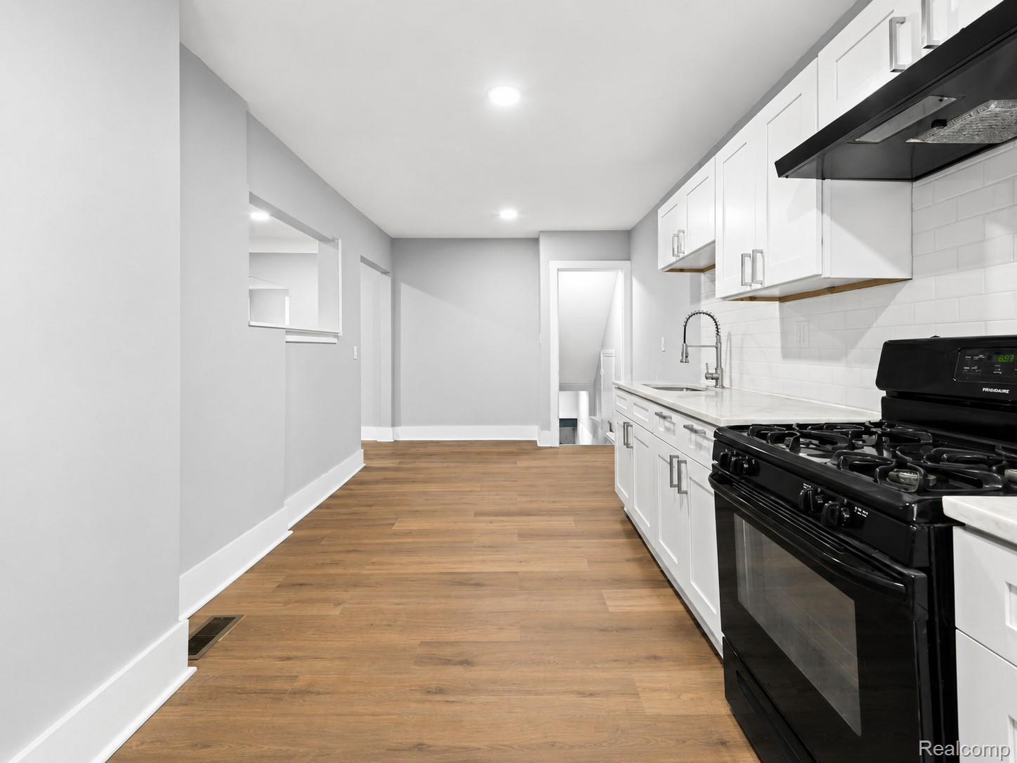 9175 Devonshire Road Detroit, MI 48224 - Photo 8 of 23 Modern kitchen featuring white shaker cabinetry, light countertops, subway tile backsplash, and a black gas range with a matching range hood