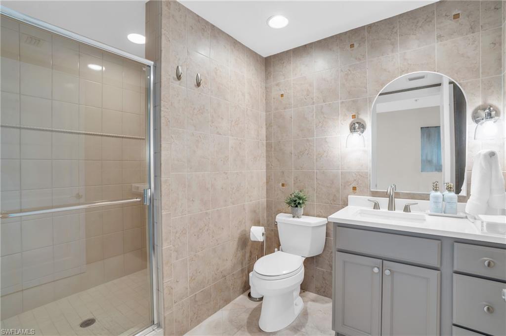 265 Indies Way, Unit 1402 Naples, FL 34110 - Photo 37 of 44 Bathroom featuring tile flooring, vanity with extensive cabinet space, an enclosed shower, tile walls, and toilet