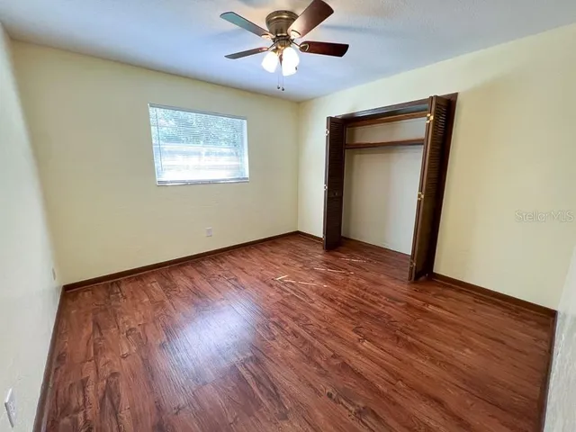 a view of an empty room with wooden floor and a ceiling fan