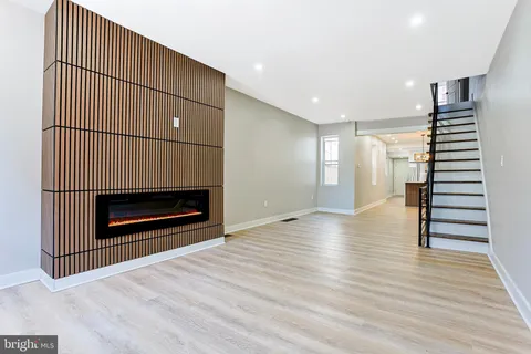 a view of an empty room with wooden floor stairs and a fireplace