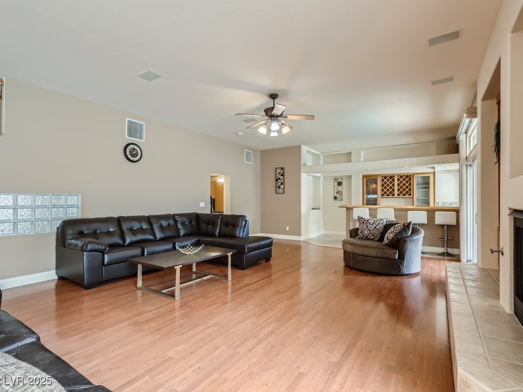 1221 Fragrant Spruce Avenue Las Vegas, NV 89123 - Photo 19 of 59 Living area with a tile fireplace, light wood-style flooring, bar area, and a ceiling fan with light