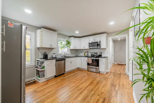 a kitchen with granite countertop a refrigerator a stove top oven a sink a dining table and chairs with wooden floor