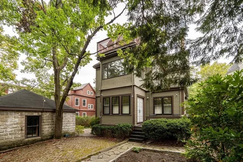 a view of a wooden house with a small yard and large trees