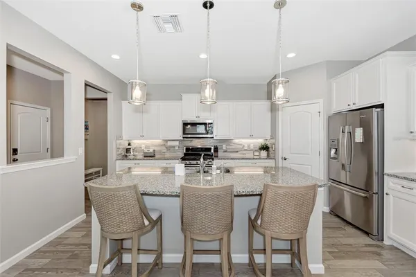 a kitchen with stainless steel appliances a refrigerator a stove a sink a dining table and chairs with wooden floor