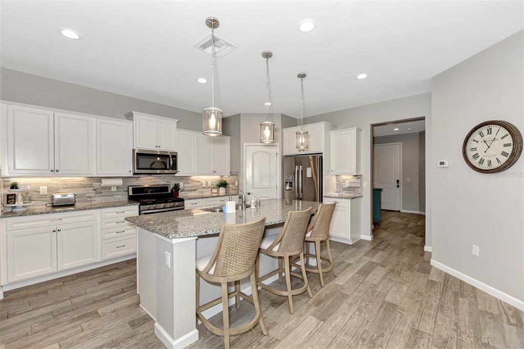 11616 Golden Bay Place Lakewood Ranch, FL 34211 - Photo 21 of 66 a kitchen with stainless steel appliances a refrigerator a stove a sink a dining table and chairs with wooden floor