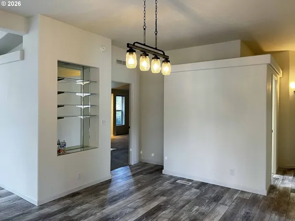 a view of a refrigerator in kitchen and an empty room with wooden floor