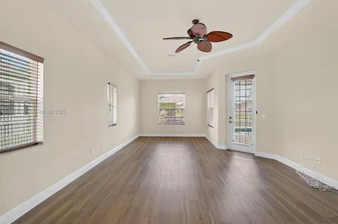 an empty room with wooden floor chandelier fan and windows