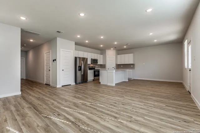 an empty room with wooden floor and kitchen view