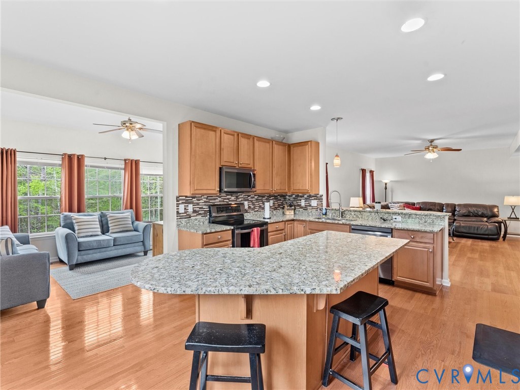 7036 Heartleaf Lane Moseley, VA 23120 - Photo 9 of 28 a kitchen with stainless steel appliances granite countertop a kitchen island a stove a dining table and chairs with wooden floor