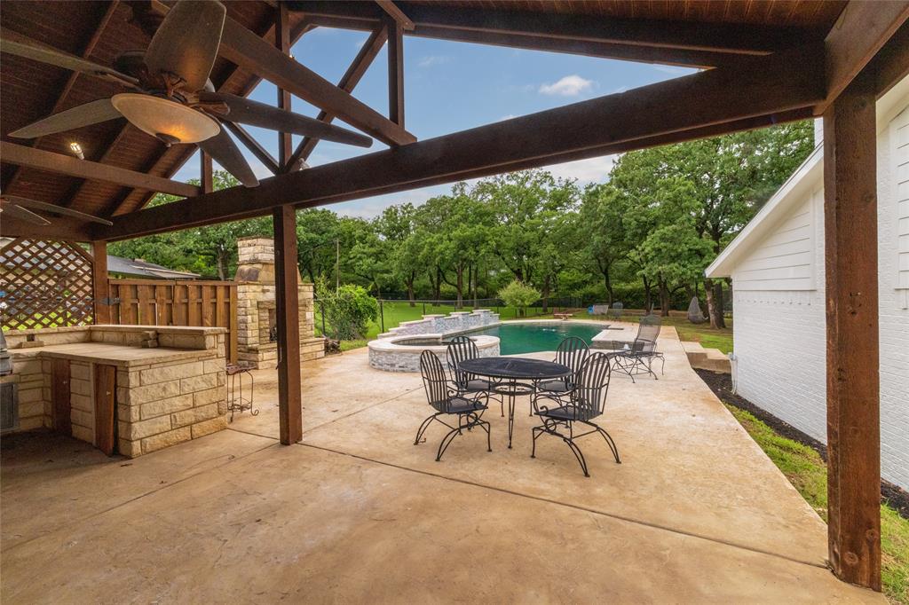 8948 David Fort Road Argyle, TX 76226 - Photo 35 of 39 Covered patio featuring an outdoor kitchen with stone base, a stone fireplace, and exposed wood beam ceiling with ceiling fans