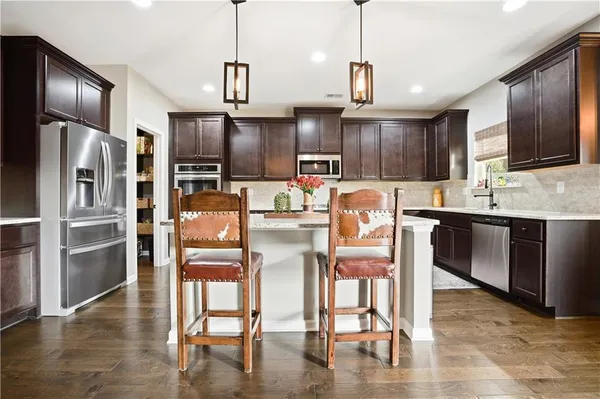 a kitchen with stainless steel appliances granite countertop a refrigerator a stove top oven a sink dishwasher and white cabinets with wooden floor