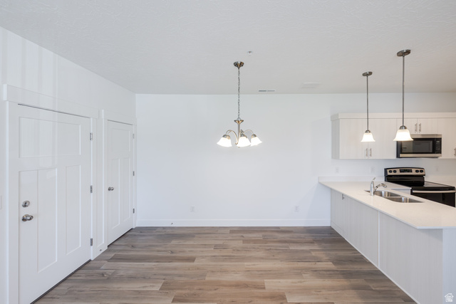 4727 South 690th West, Unit W202 Mapleton, UT 84664 - Photo 5 of 16 Open-concept living area with wood-finish flooring, white cabinetry, integrated stainless steel appliances, and pendant lighting
