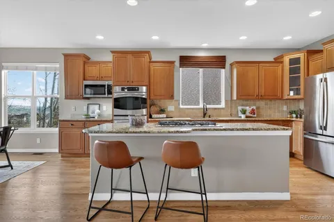 a kitchen with stainless steel appliances granite countertop a stove top oven a sink dishwasher a refrigerator and a dining table with wooden floor