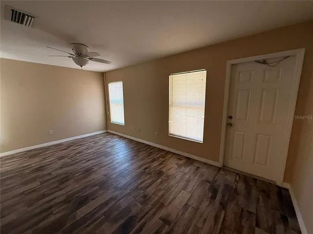 an empty room with wooden floor ceiling fan and windows