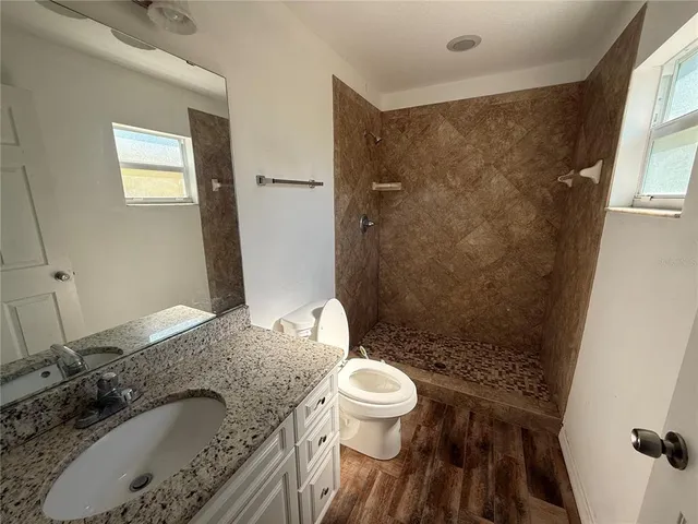 a bathroom with a granite countertop sink a toilet a mirror and shower