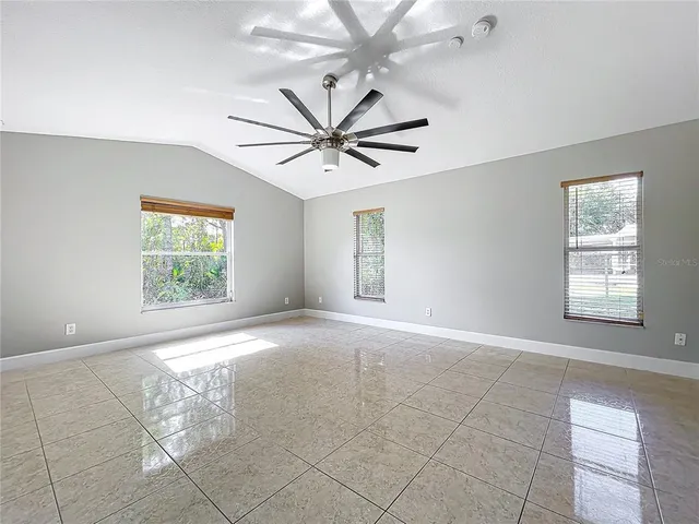 an empty room with chandelier fan and windows