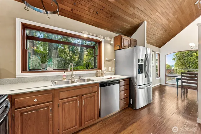 a kitchen with stainless steel appliances granite countertop a refrigerator a sink dishwasher a stove and white countertops with wooden floor