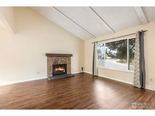 a view of an empty room with wooden floor fireplace and a window
