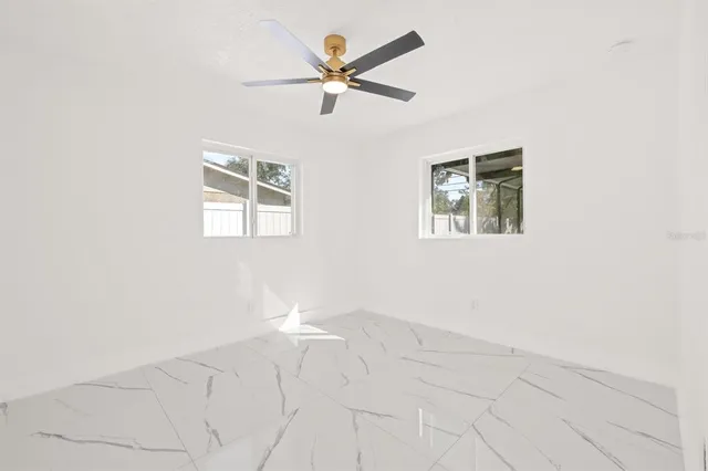 an empty room with chandelier fan and windows