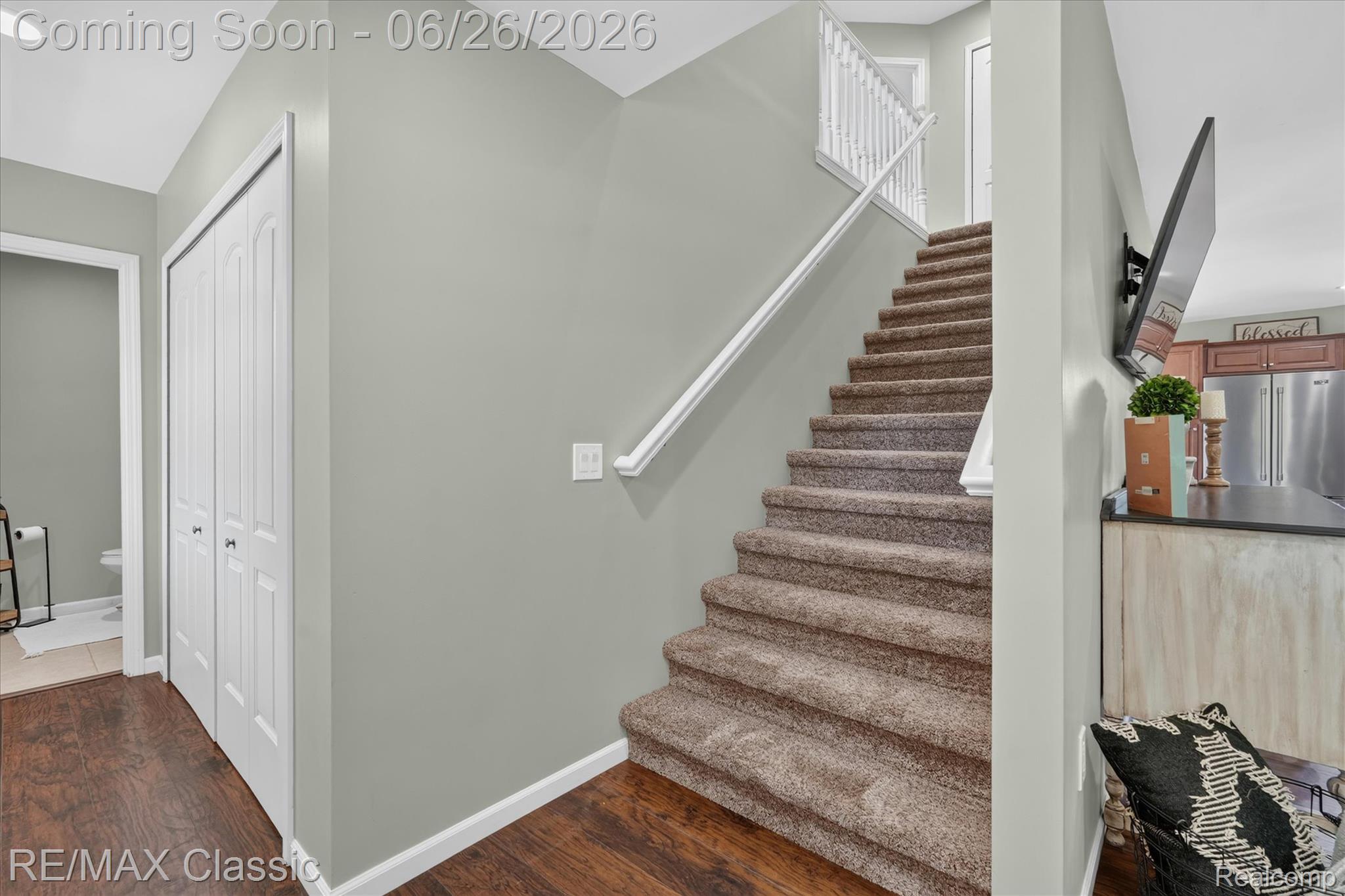 3205 North Milford Road Highland, MI 48357 - Photo 5 of 53 Carpeted staircase with white balusters and handrail, hardwood-style flooring, a bifold closet, and a partial view of a kitchen with stainless steel appliances