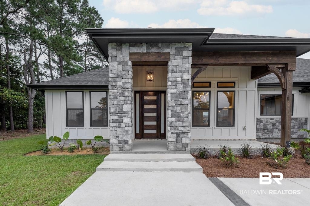 13066 Gopher Court Elberta, AL 36530 - Photo 2 of 38 Exterior featuring stone accents, board and batten siding, dark framed windows, a wooden entry door with horizontal glass panels, and exposed timber architectural elements.