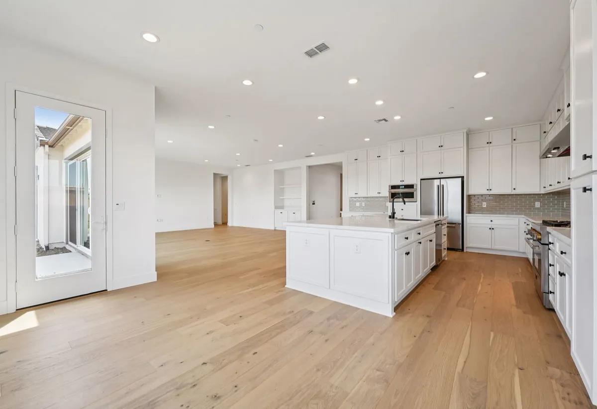 475 Trellis Way Brentwood, CA 94513 - Photo 4 of 16 a large white kitchen with kitchen island a sink a center island stainless steel appliances and a counter top space