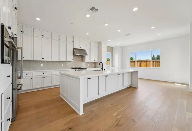 a large kitchen with stainless steel appliances granite countertop a stove a sink a refrigerator and white cabinets with wooden floor