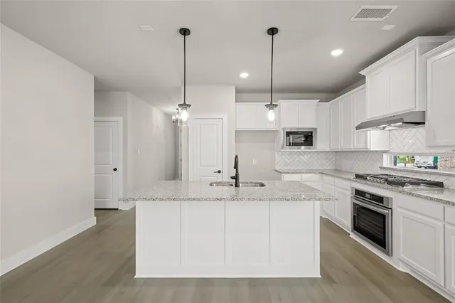 a kitchen with stainless steel appliances granite countertop a sink a stove a refrigerator and white cabinets