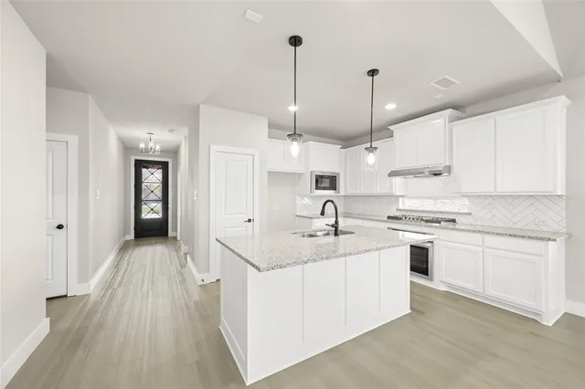 a kitchen with stainless steel appliances granite countertop a sink a stove a refrigerator and white cabinets