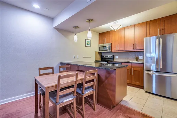 a kitchen with stainless steel appliances granite countertop a stove a refrigerator a sink a dining table and chairs with wooden floor