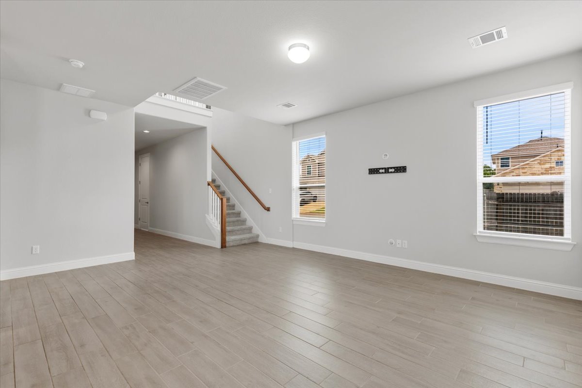 101 Free Stone Drive Georgetown, TX 78628 - Photo 11 of 40 Spacious living area featuring wood-finish flooring, light gray walls, two large windows with blinds, and a staircase with wood handrails and carpeted treads