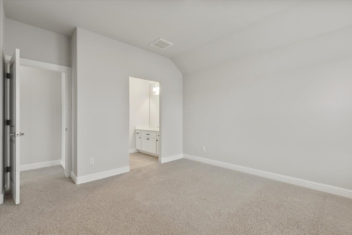101 Free Stone Drive Georgetown, TX 78628 - Photo 12 of 40 Carpeted room featuring a white baseboard, a vaulted ceiling, and an open doorway to a vanity area with a built-in cabinet