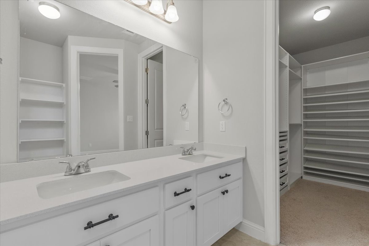 101 Free Stone Drive Georgetown, TX 78628 - Photo 16 of 40 Dual vanity with integrated sinks, white cabinetry, and matte black hardware, accompanied by a custom walk-in closet featuring extensive built-in shelving and drawers