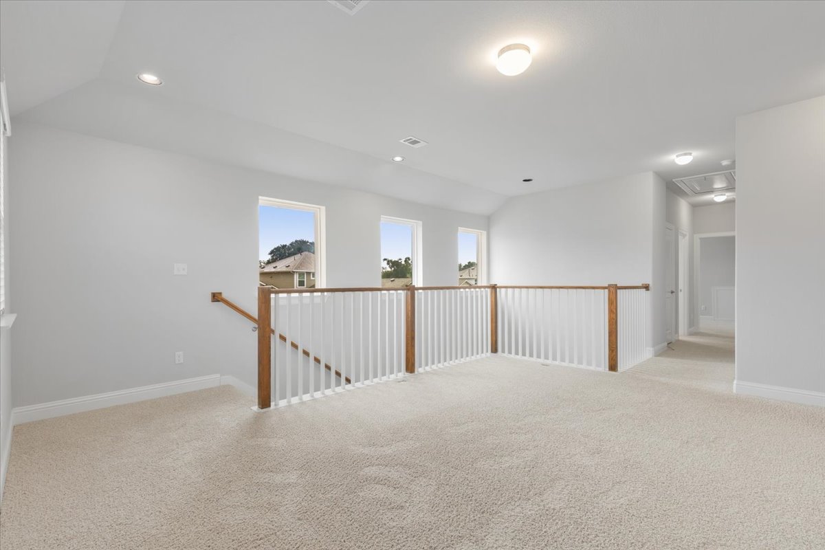 101 Free Stone Drive Georgetown, TX 78628 - Photo 19 of 40 Spacious carpeted loft area featuring a white baluster railing with wood-finish top rail, multiple windows, recessed lighting, and a ceiling-mounted light fixture